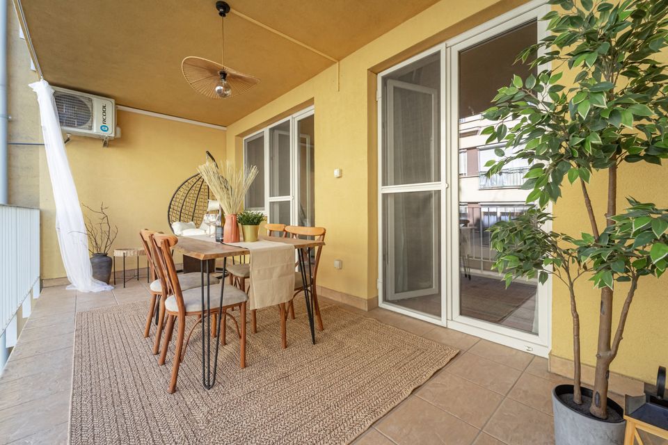 A loggia most: étkezőasztal fa székekkel, függőfotel, szőnyeg