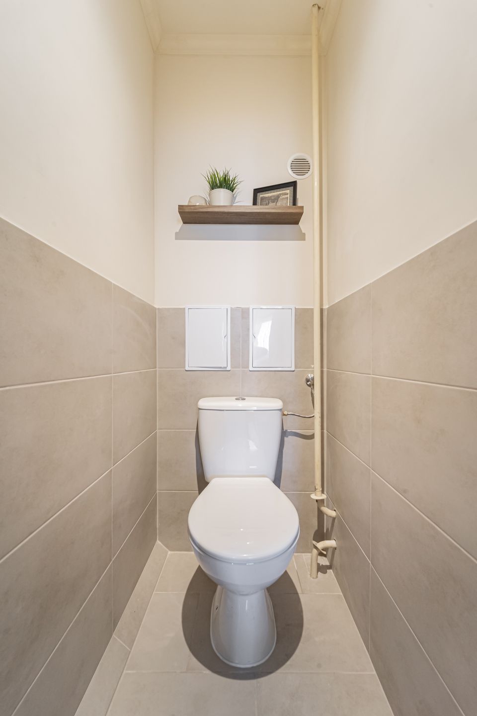 A WC a felújítás után: burkolt fal, eltakart strang, polc